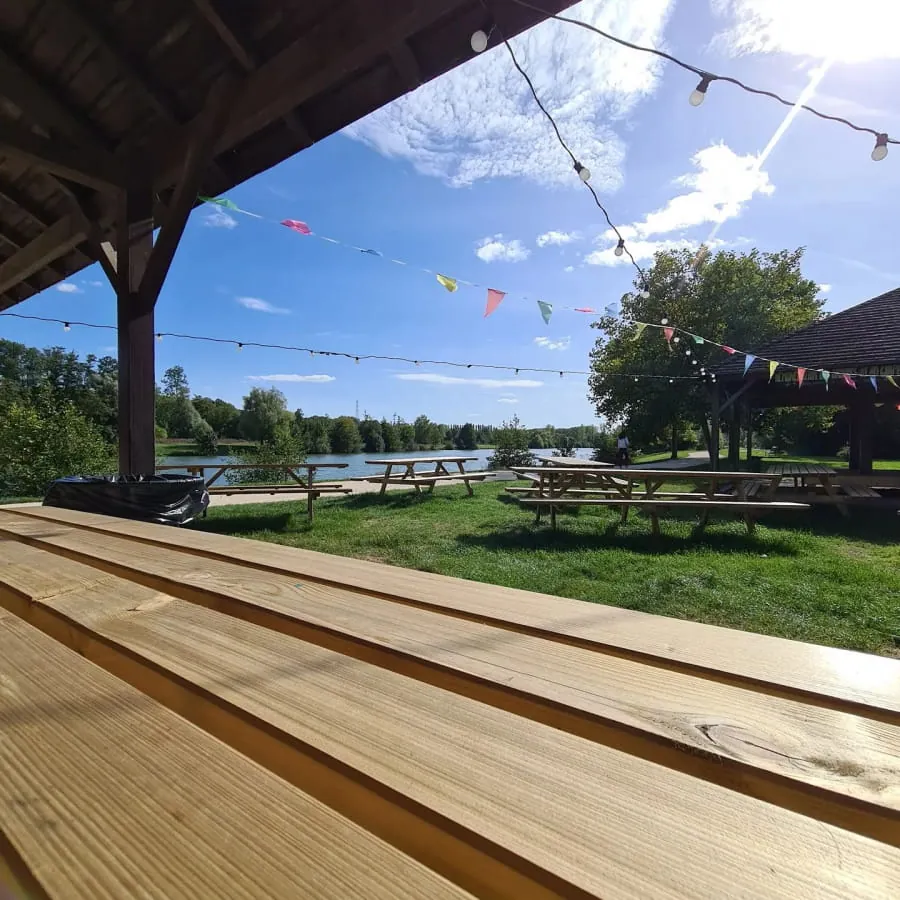 Tables en bois face au lac de Luisant, sous les guirlandes de la guinguette