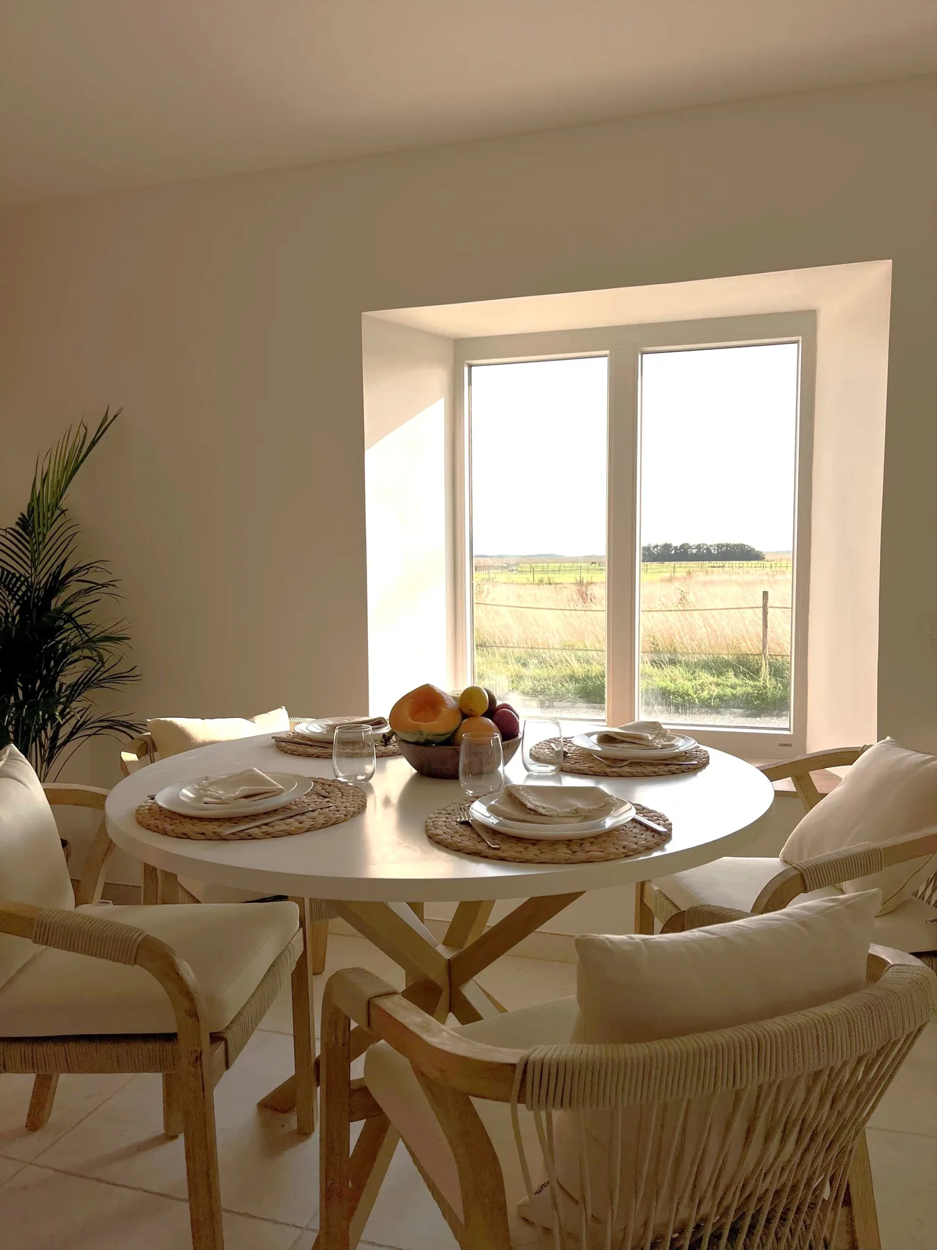 Round table set for breakfast, facing the window onto the fields